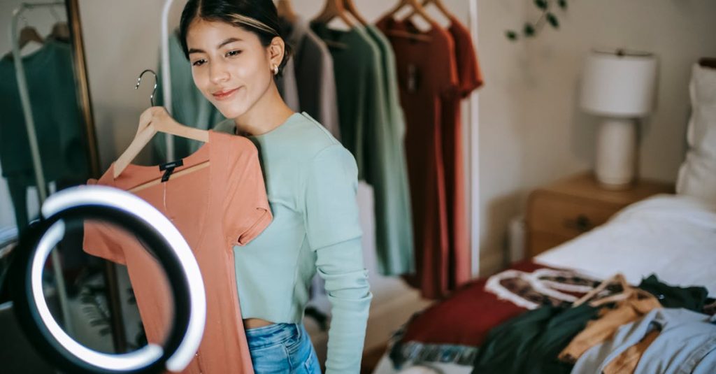 A young woman presenting outfits for a social media fashion video in her stylish bedroom.